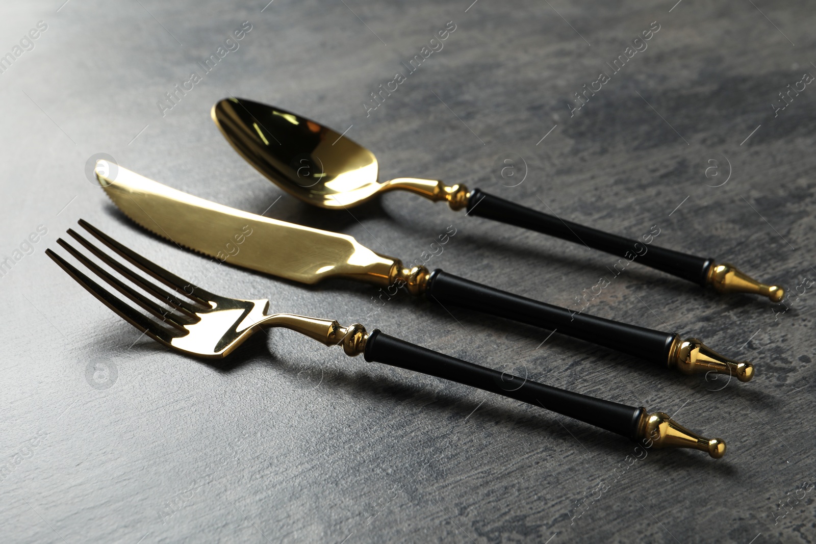 Photo of Elegant golden cutlery set on dark grey table