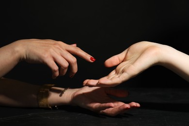 Photo of Fortune teller reading lines on woman's palm at dark grey table, closeup. Chiromancy