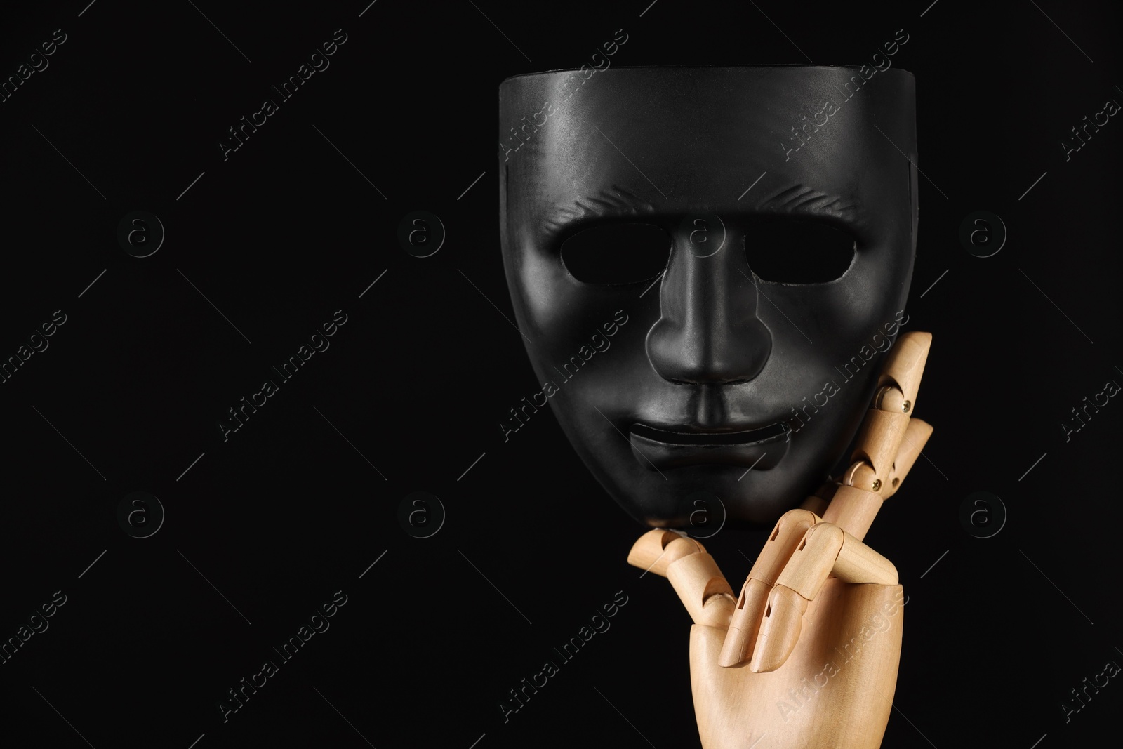 Photo of Wooden mannequin hand holding plastic mask on black background, space for text. Theatrical performance