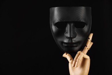 Photo of Wooden mannequin hand holding plastic mask on black background, space for text. Theatrical performance