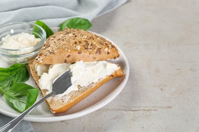 Pieces of bread with cream cheese and basil leaves on light gray textured table, closeup. Space for text