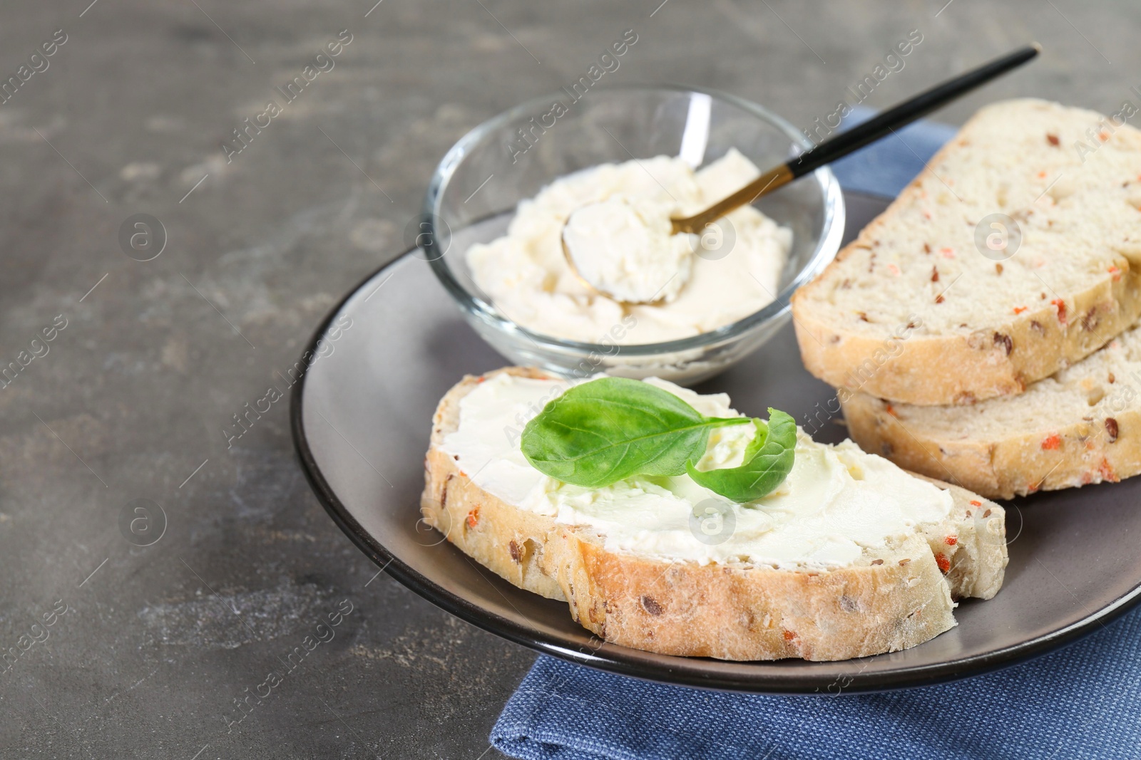 Photo of Pieces of bread with cream cheese and basil leaves on gray textured table, closeup. Space for text