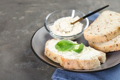 Pieces of bread with cream cheese and basil leaves on gray textured table, closeup. Space for text