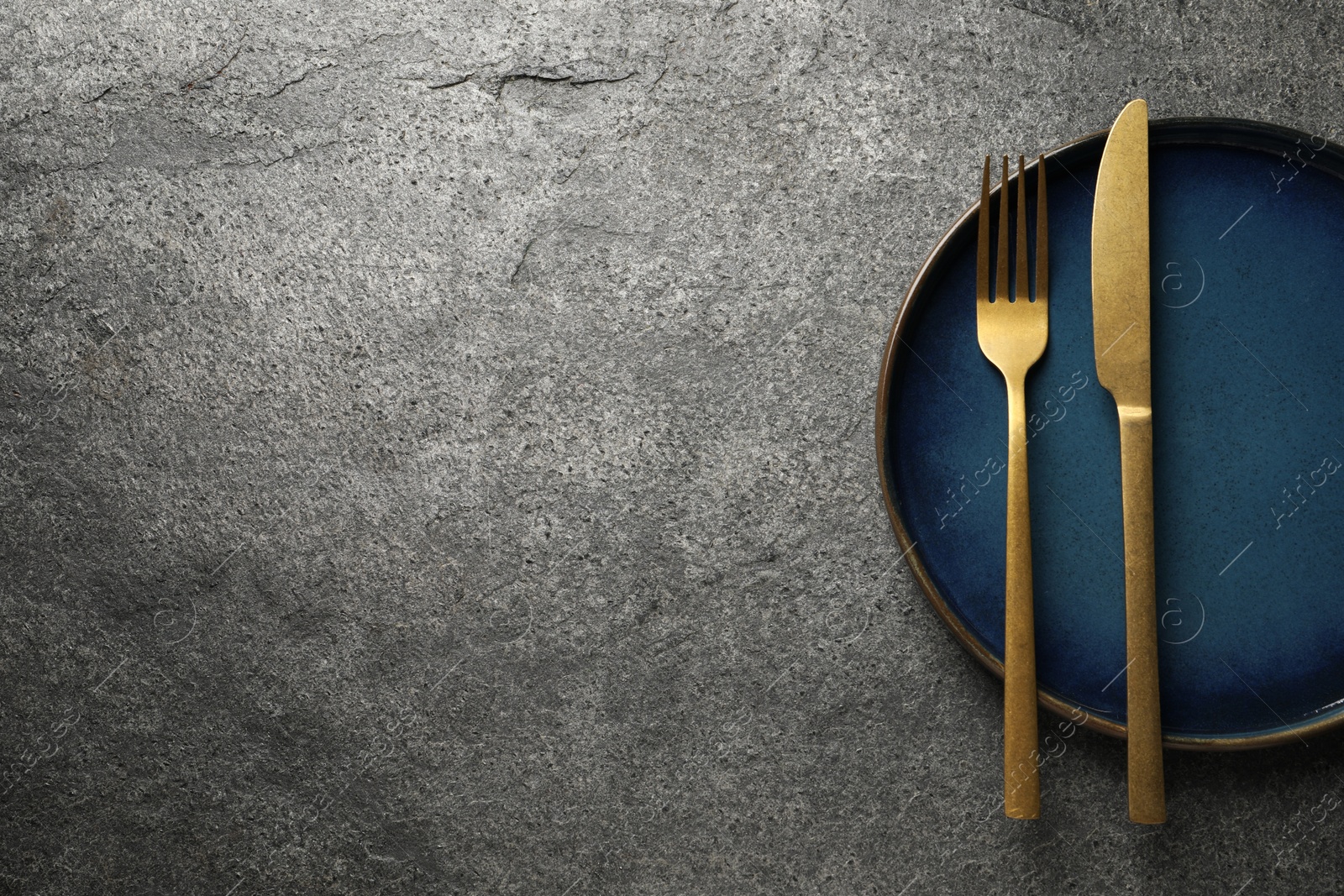 Photo of Stylish golden cutlery and plate on grey table, top view. Space for text