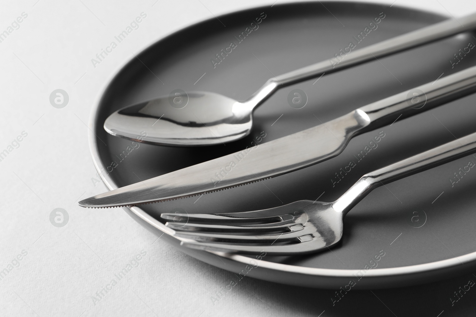 Photo of Stylish silver cutlery and plate on white background, closeup