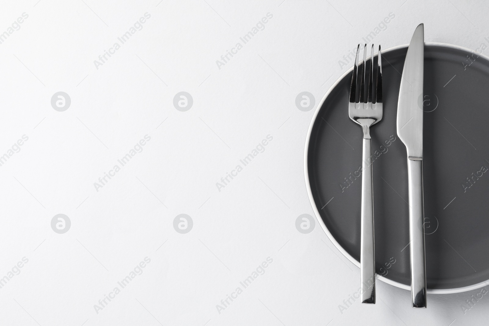 Photo of Stylish silver cutlery and plate on white background, top view. Space for text