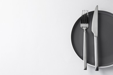 Stylish silver cutlery and plate on white background, top view. Space for text