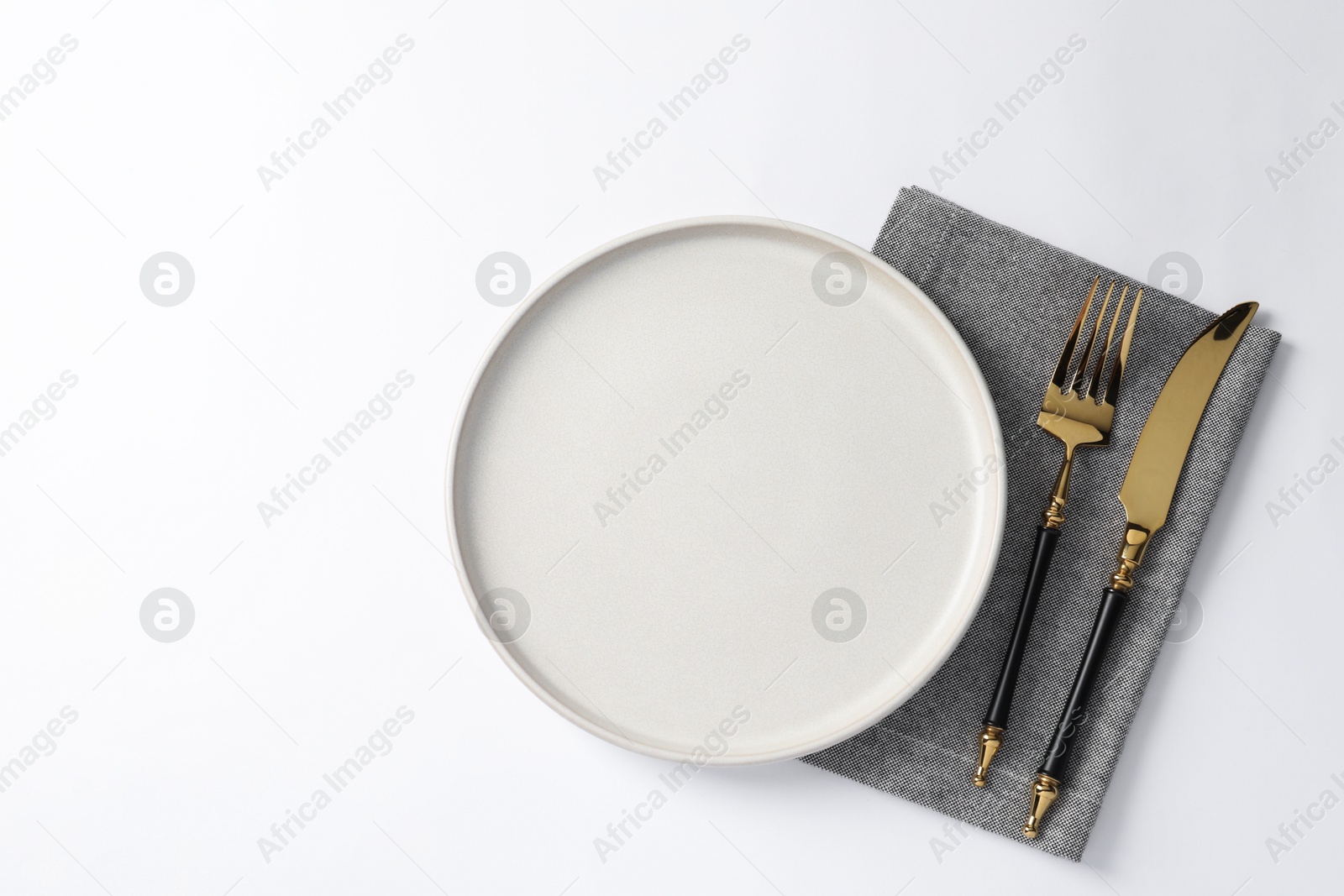 Photo of Stylish golden cutlery, plate and napkin on white background, top view. Space for text