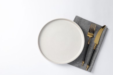 Stylish golden cutlery, plate and napkin on white background, top view. Space for text