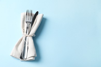 Stylish silver cutlery and napkin on light blue background, top view. Space for text