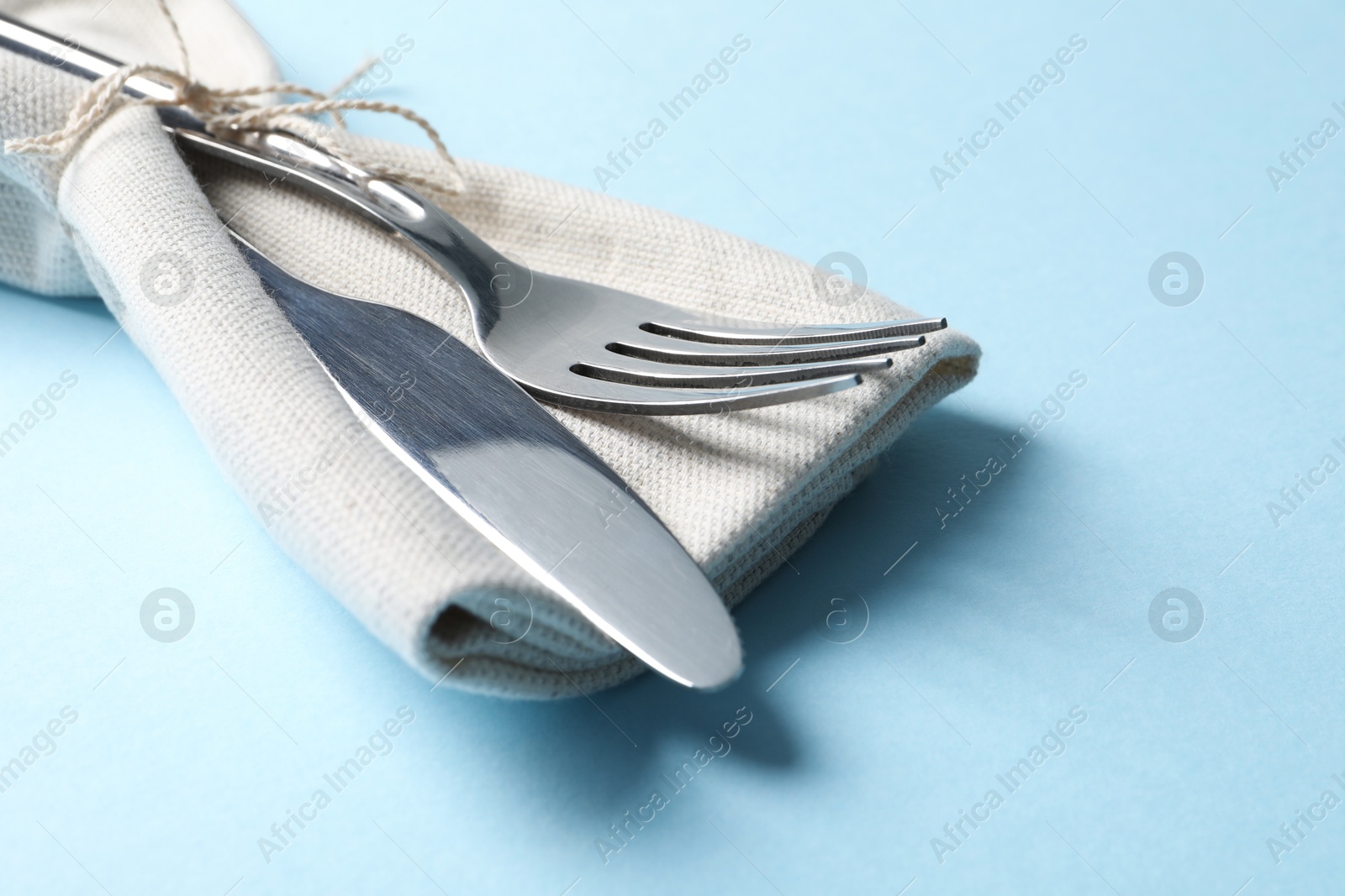 Photo of Stylish silver cutlery and napkin on light blue background, closeup