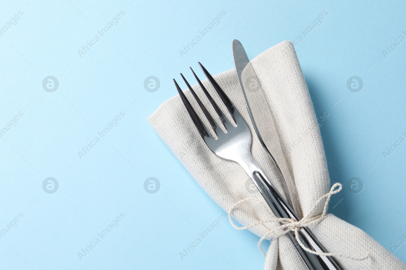 Photo of Stylish silver cutlery and napkin on light blue background, top view. Space for text