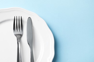 Photo of Stylish silver cutlery and plate on light blue background, top view. Space for text