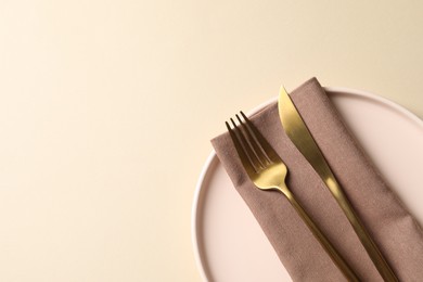 Photo of Stylish golden cutlery, plate and napkin on beige background, top view. Space for text