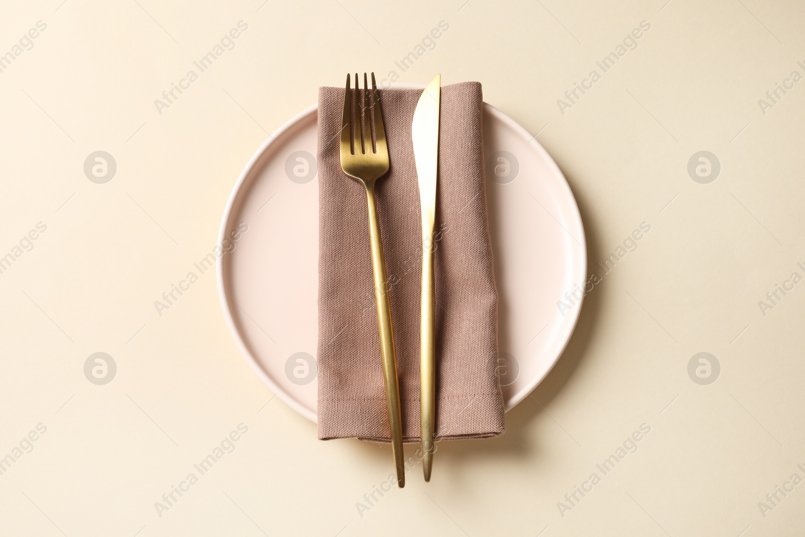 Photo of Stylish golden cutlery, plate and napkin on beige background, top view