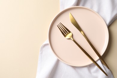 Photo of Stylish golden cutlery, plate and napkin on beige background, top view. Space for text