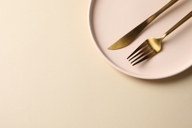 Photo of Stylish golden cutlery and plate on beige background, top view. Space for text