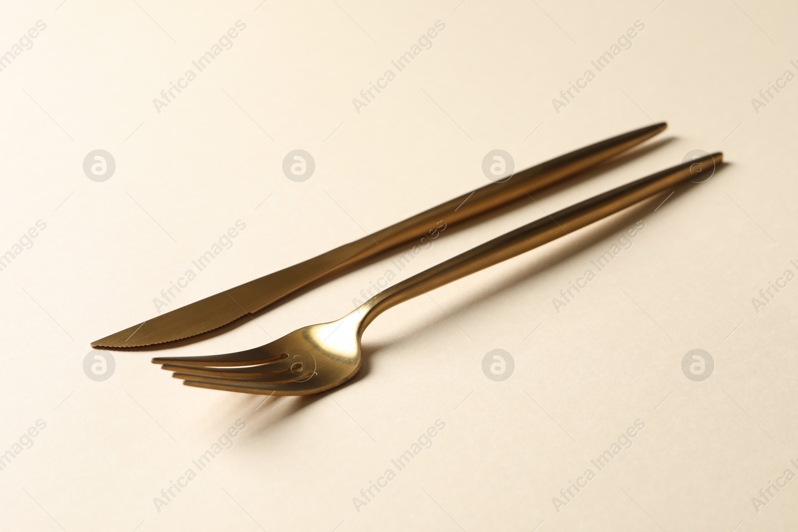 Photo of Stylish golden cutlery. Fork and knife on beige background