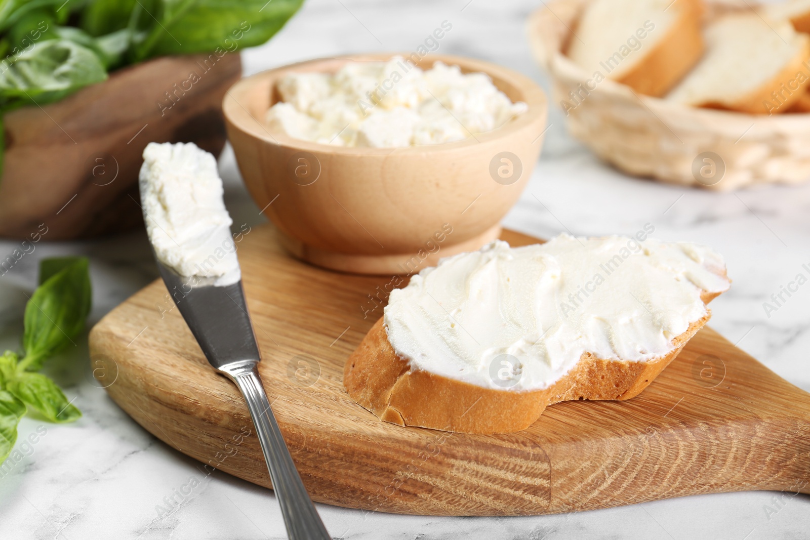 Photo of Piece of bread with cream cheese and knife on white marble table