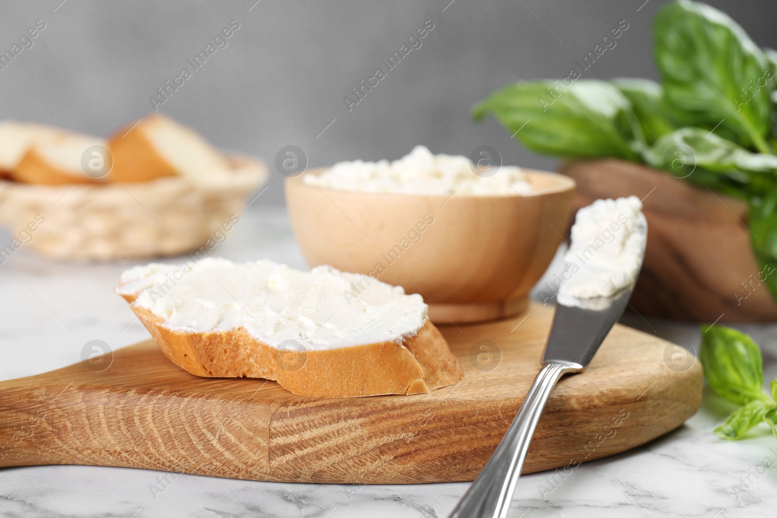 Photo of Piece of bread with cream cheese and knife on white marble table