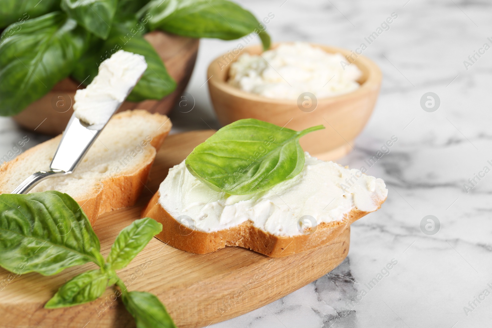 Photo of Pieces of bread with cream cheese and basil leaves on white marble table