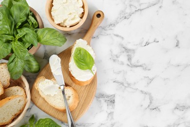 Pieces of bread with cream cheese and basil served on white marble table, flat lay. Space for text