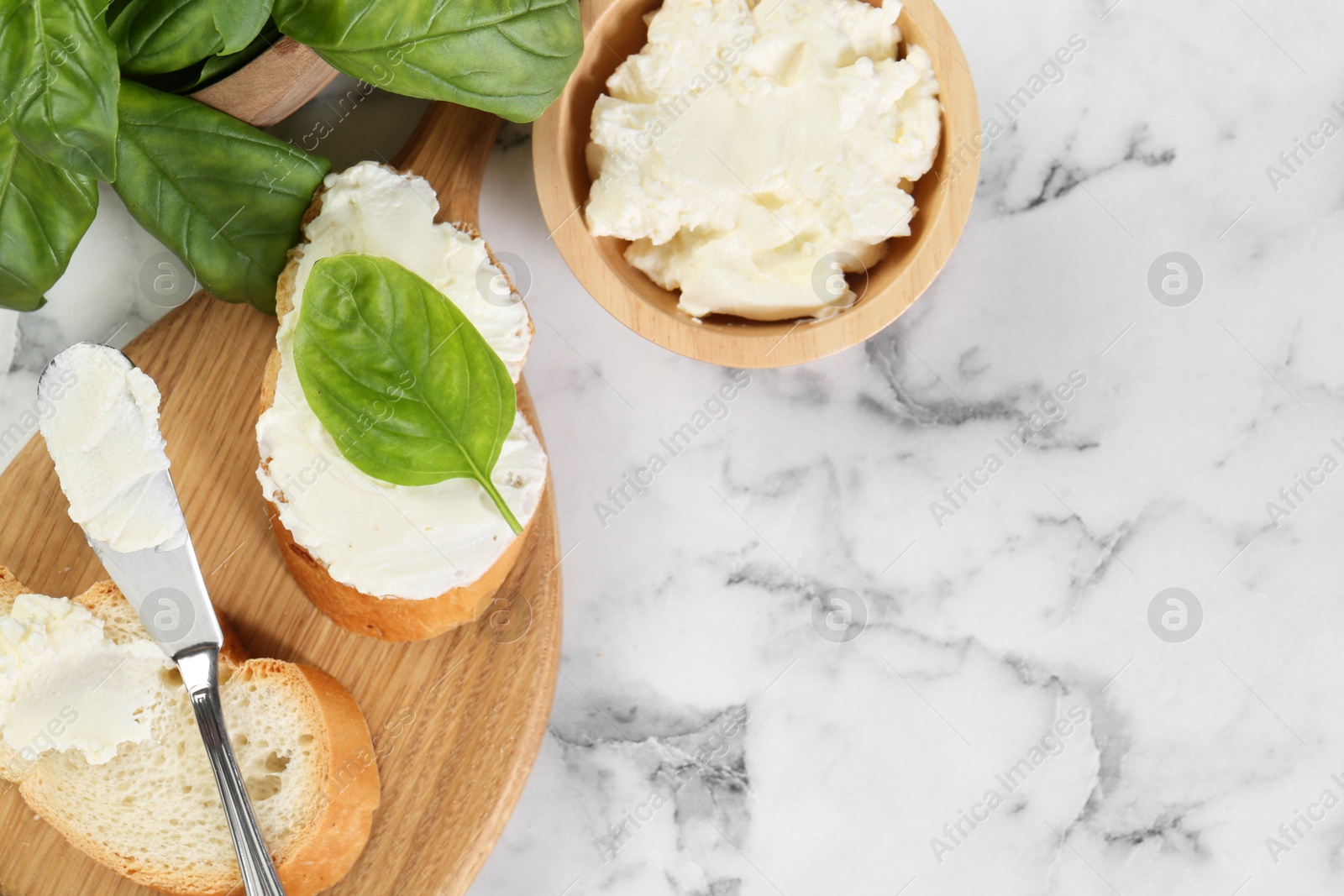 Photo of Pieces of bread with cream cheese and basil served on white marble table, flat lay. Space for text