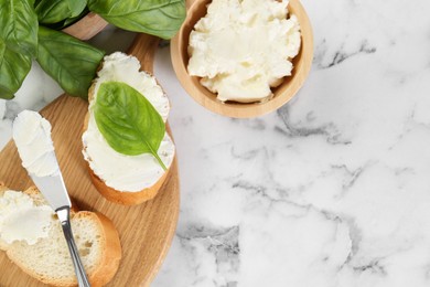 Photo of Pieces of bread with cream cheese and basil served on white marble table, flat lay. Space for text