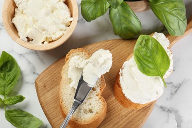 Photo of Pieces of bread with cream cheese and basil served on white marble table, flat lay