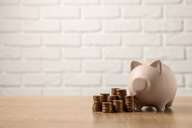 Piggy bank and stacks of coins on wooden table, space for text