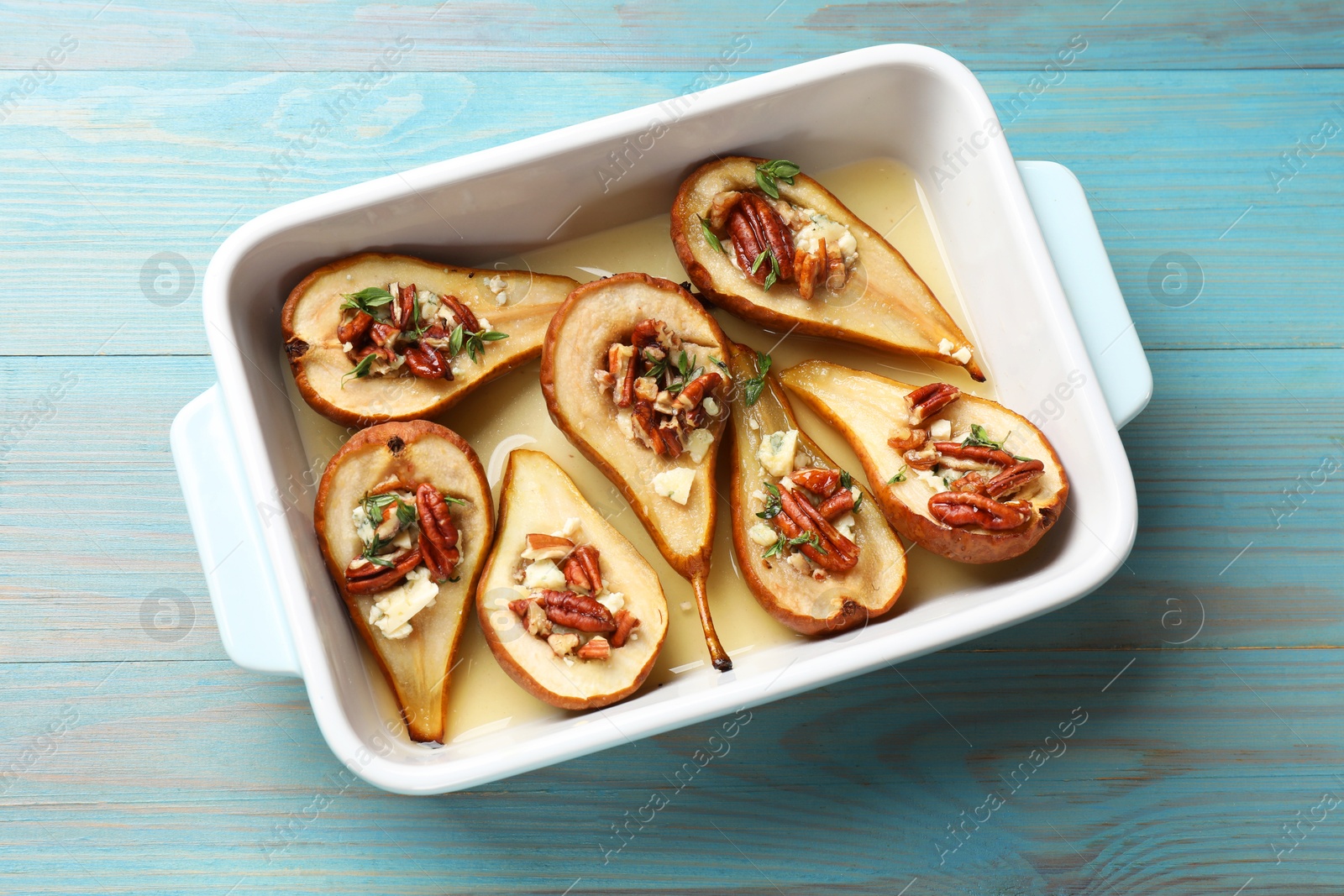 Photo of Delicious baked pears with nuts, blue cheese, thyme and honey in baking dish on light blue wooden table, top view