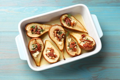 Delicious baked pears with nuts, blue cheese, thyme and honey in baking dish on light blue wooden table, top view