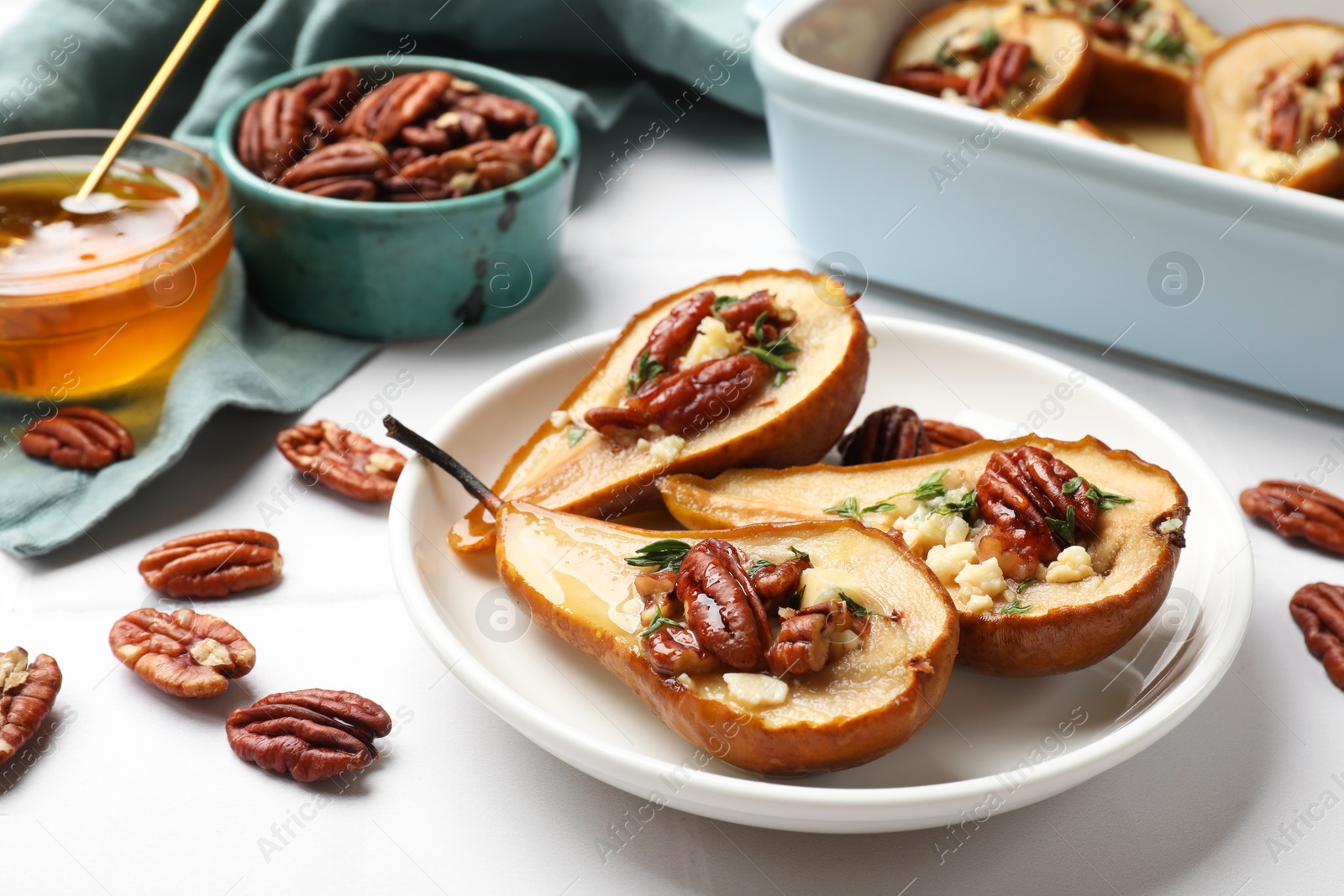 Photo of Delicious baked pears with nuts, blue cheese, thyme and honey on white table