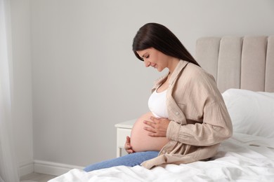 Beautiful pregnant woman on bed at home, space for text