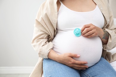 Photo of Pregnant woman with light blue pacifier at home, closeup. Space for text