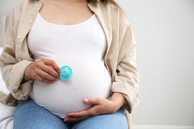 Photo of Pregnant woman with light blue pacifier on gray background, closeup. Space for text