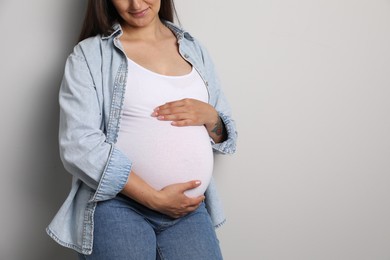 Photo of Pregnant woman on gray background, closeup. Space for text