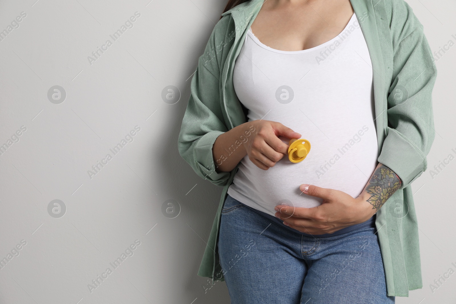 Photo of Pregnant woman with yellow pacifier on gray background, closeup. Space for text