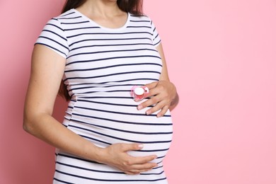 Photo of Pregnant woman with pacifier on pink background, closeup. Space for text