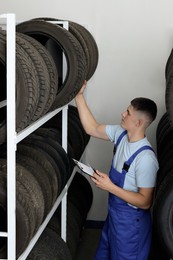 Photo of Young man with clipboard near car tires in auto store