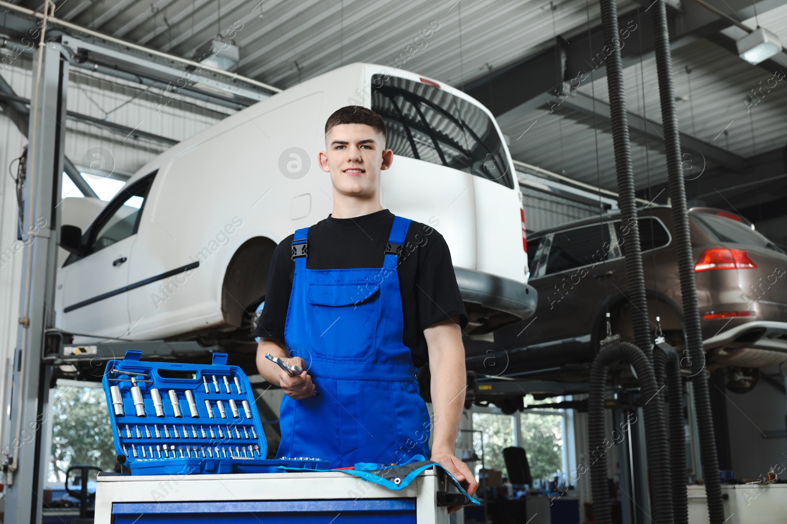 Photo of Young auto mechanic with different tools at automobile repair shop, low angle view