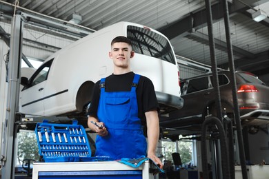 Photo of Young auto mechanic with different tools at automobile repair shop, low angle view