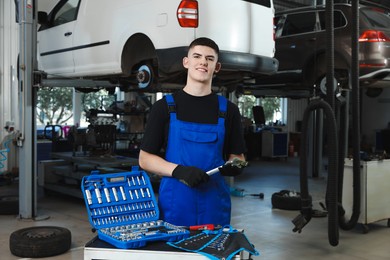 Photo of Young auto mechanic with different tools at automobile repair shop