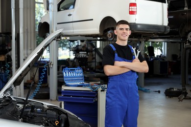 Young auto mechanic near broken car at automobile repair shop