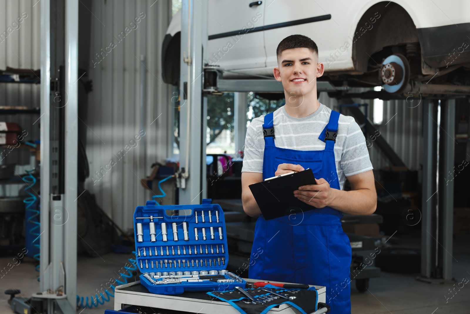 Photo of Young auto mechanic with clipboard taking notes near broken car at automobile repair shop