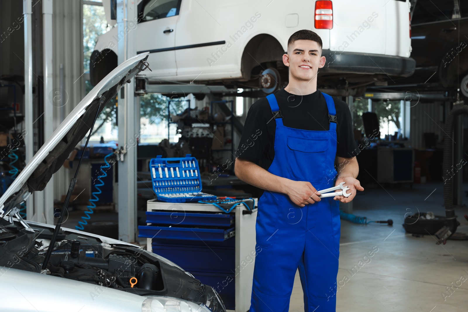 Photo of Young auto mechanic with wrenches near broken car at automobile repair shop