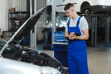 Photo of Young auto mechanic taking notes while doing car diagnostic at automobile repair shop