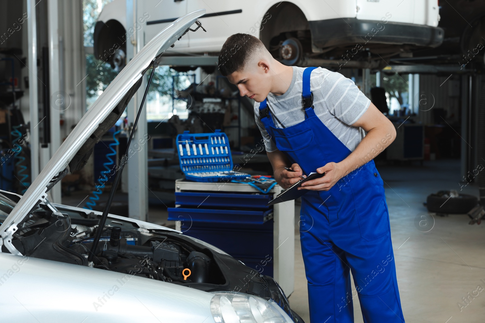 Photo of Young auto mechanic taking notes while doing car diagnostic at automobile repair shop