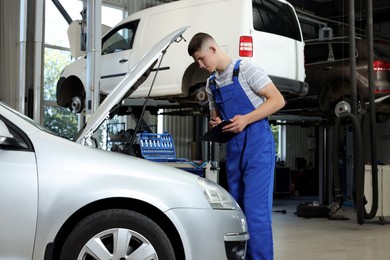 Photo of Young auto mechanic taking notes while doing car diagnostic at automobile repair shop