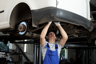 Photo of Young auto mechanic fixing lifted car at automobile repair shop